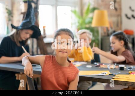 Ritratto di contenuto ragazza asiatica seduta contro insegnante e bambini Alla classe di artigianato di Halloween Foto Stock