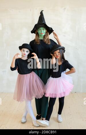 Ritratto di donna verde grave in streghe cappello in posa con cute ragazze mime grimacing contro parete grigia Foto Stock