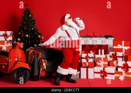 Foto a lunghezza intera di Crazy babbo natale cantare canzone in microfono isolato su sfondo rosso lucido con calze x-mas caminetto Foto Stock