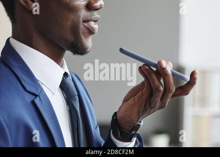 Primo piano di uomo africano in tuta che tiene il telefono cellulare e. parlare o registrare un messaggio audio Foto Stock