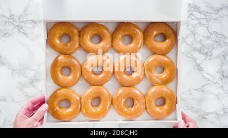 Disposizione piatta. Semplici ciambelle smaltate acquistate in una scatola di carta bianca. Foto Stock