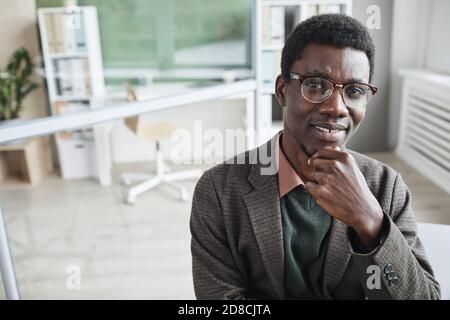Ritratto di giovane lavoratore d'ufficio africano in suit sorridente a. fotocamera mentre si lavora in ufficio Foto Stock