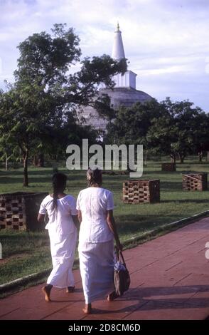 Due pellegrini vestiti in bianco camminando nell'antica città sacra buddista di Anuradhapura, Sri Lanka Foto Stock