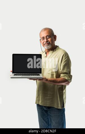 Uomo adulto o nonno indiano asiatico senior che presenta un notebook vuoto schermo su sfondo bianco Foto Stock