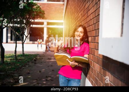 Studente indiano asiatico del college a fuoco lavorando su laptop o leggere il libro, mentre altri compagni di classe in background, immagine all'aperto nel campus universitario Foto Stock