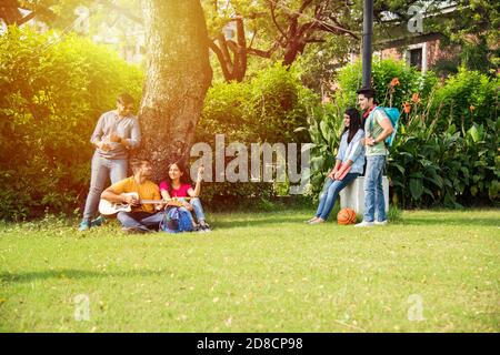 Gli studenti del college indiano asiatico suonano musica con la chitarra mentre si siedono nel campus, sulle scale o sul prato Foto Stock