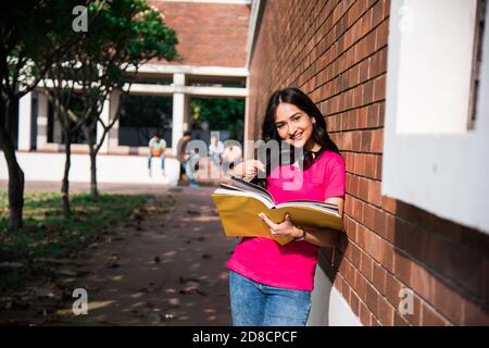 Studente indiano asiatico del college a fuoco lavorando su laptop o leggere il libro, mentre altri compagni di classe in background, immagine all'aperto nel campus universitario Foto Stock