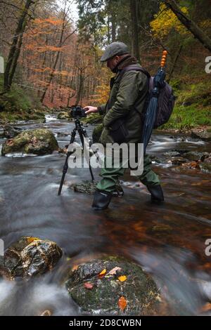 Fotografo con macchina fotografica e treppiede nel fiume Hogne in alta fens, Belgio, Wallonie, Ardenne, Hockai Foto Stock