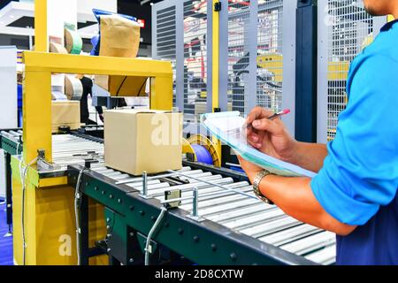 Manager engineer verifica scatole di cartone su nastro trasportatore in magazzino di distribuzione. Concetto di sistema di trasporto pacchi. Foto Stock