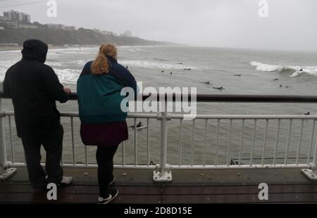 La gente guarda fuori dal molo di Bournemouth mentre i surfisti si godono le grandi onde nel mare al largo della spiaggia di Bournemouth in Dorset. Il Met Office ha avvertito che i downpour torrenziali sono previsti per portare 'infuori' in tutto il Regno Unito con grandi onde, pioggia pesante, forti galee e potenziali inondazioni fluviali che colpiscono la costa occidentale dell'Inghilterra, gran parte del Galles e parti della Scozia da giovedì. Foto Stock