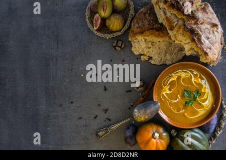 Zuppa di zucca con pane appena sfornato e cucchiaio d'argento su tavola grigia. Foto dall'alto del pasto vegano. Concetto di alimentazione sana. Foto Stock