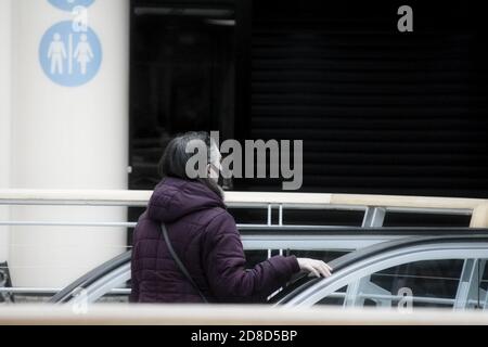 Donna nella scala mobile del centro commerciale con la sua maschera sul viso. Foto Stock