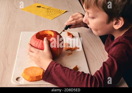 Halloween, decorazione e idee di vacanza - primo piano di capretto con la zucca di intaglio del coltello o jack-o-lanterna. il ragazzo di 6 anni ha attività di divertimento casalinga. Mamma Foto Stock