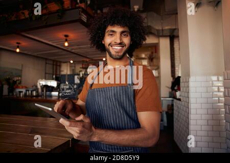 Ritratto di bel giovane cameriere maschio in piedi in un bar che indossa grembiule per tablet digitale Foto Stock