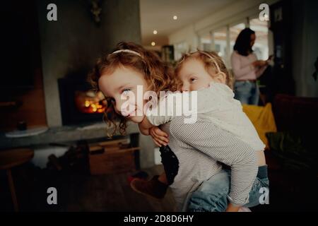 Carino bambina che dà a sorella più giovane un giro piggyback a. casa Foto Stock