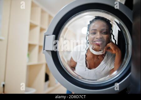 Divertente ritratto di allegra donna afroamericana vicino lavatrice nella lavanderia self-service. Foto Stock