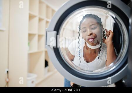 Divertente ritratto di allegra donna afroamericana vicino lavatrice nella lavanderia self-service. Foto Stock