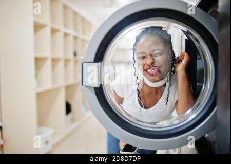 Divertente ritratto di allegra donna afroamericana vicino lavatrice nella lavanderia self-service. Foto Stock