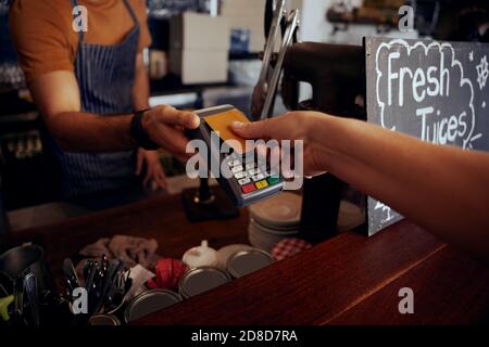 Mani femminili che tengono la carta contro la macchina di pagamento nfs per fare pagamento per acquisto in caffetteria Foto Stock