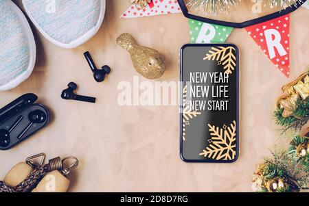 New Year Resolutions obiettivi sani concetto di fondo. New Year New Life New Start testo sul telefono cellulare sul tavolo con scarpe sportive, auricolare wireless, Foto Stock