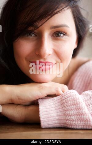 Primo piano ritratto di donna bianca sorridente appoggiata al tavolo a casa Foto Stock