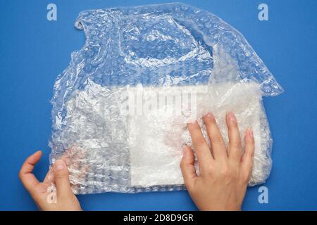 due mani femminili stanno avvolgendo l'articolo in un involucro di plastica trasparente con bolle, sfondo blu Foto Stock