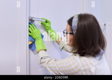 Donna che pulisce e lucida la porta bianca e la maniglia cromata con straccio Foto Stock