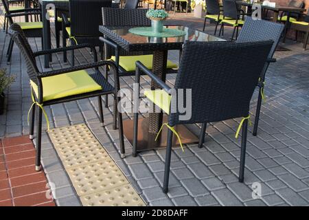 Tavolo quadrato con tela verde decorativa rotonda e fiori e. sedie in vimini nero con cuscini gialli sulle vicinanze caffetteria all'aperto sul marciapiede in piastrelle Foto Stock