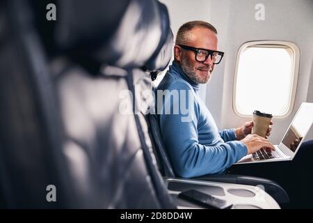Uomo d'affari soddisfatto in occhiali seduto nella cabina dell'aeromobile Foto Stock
