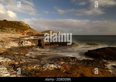 Le onde si infrangono sulla costa della baia di Bracelet sul Mumbles, Swansea crogiolati in colori solari Foto Stock