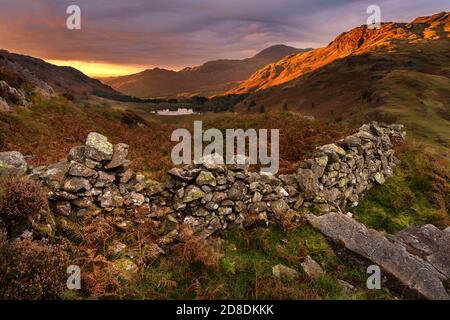 Splendida alba con prima luce sulle cime delle montagne su Side Pike nel Lake District, Regno Unito. Un vecchio muro di pietra può essere visto in primo piano. Foto Stock