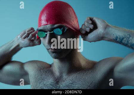 Primo piano nuotatore maschio caucasico professionista che si prepara per l'allenamento isolato su sfondo blu di studio neoned. Grazia del movimento e dell'azione. Stile di vita sano, sport e concetto di movimento. Foto Stock