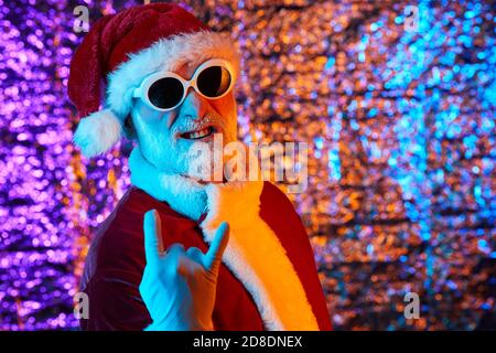 Ritratto di Babbo Natale in costume rosso e occhiali da sole in posa sulla fotocamera contro lo sfondo lucido Foto Stock