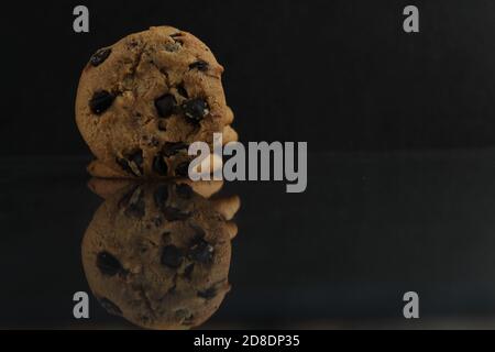 biscotti di fondo del cibo rotondi con gocce di cioccolato stesi sopra il bordo del bordo con un riflesso su a. nero scuro specchio vista laterale Foto Stock