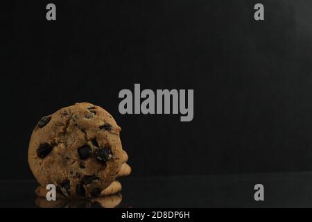 biscotti di fondo del cibo rotondi con gocce di cioccolato stesi sopra il bordo del bordo con un riflesso su a. nero scuro specchio vista laterale Foto Stock