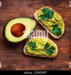 Avocado su vecchio tavolo di legno, spazio copia. Sandwich di avocado su pane di segale scuro Vista dall'alto. Foto Stock