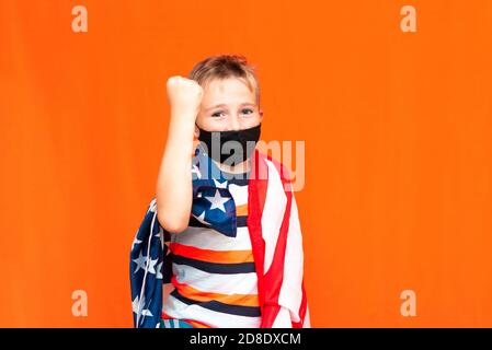 Ragazzo calmo indossando maschera nera come pugile sopra la bandiera usa a spalla su sfondo arancione Foto Stock