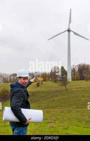 Lavoratore maschile indicando nuova area per costruire eolico fattoria e. impianto fotovoltaico site.autumn prato verde cielo nuvoloso all'aperto Foto Stock