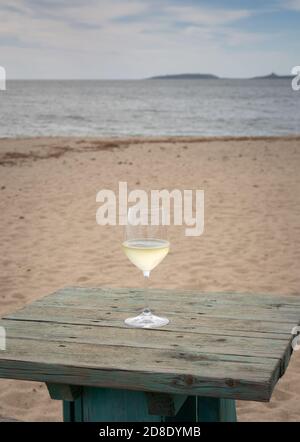 Bicchiere di prosecco su un tavolo sulla spiaggia di Torregrande, nel centro della Sardegna Foto Stock