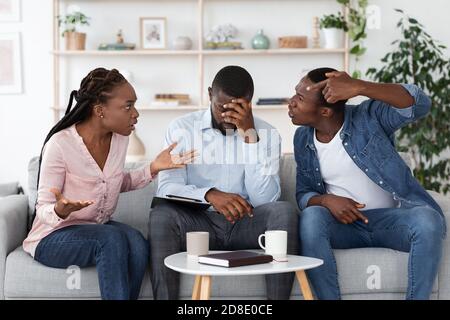 Psicoterapeuta stanco seduto sul lettino tra le coppie in lite durante la terapia Sessione Foto Stock