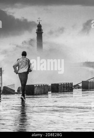 Corsa fredda - uomo che corre in una tempesta come onde crash sopra il faro Foto Stock