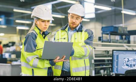 Lavoratore industriale maschile e ingegnere meccanico capo femminile a piedi Attraverso lo stabilimento di produzione mentre discutono il nuovo progetto e l'uso della fabbrica Computer portatile Foto Stock