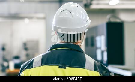 Indietro Vista Foto dell'ingegnere industriale che indossa indumenti protettivi Attraversa il moderno stabilimento di produzione con macchine automatiche in funzione Foto Stock