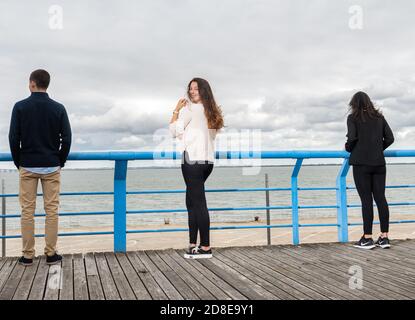 Tre persone si distinguono su una passerella, di fronte all'oceano sotto un cielo nuvoloso, trasmettendo solitudine e contemplazione. Foto Stock