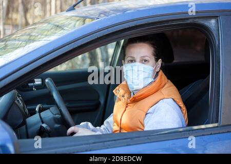 Bella giovane donna felice è pronta a guidare la sua nuova auto con maschera protettiva sul viso Foto Stock