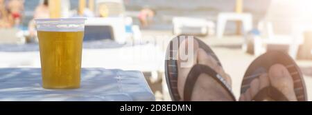 Ragazzo in piedi sulla sdraio spiaggia sedia rilassante e bere un fresca birra fredda viaggio vacanza caldo tempo Foto Stock