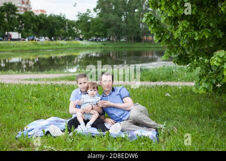 Un solo padre con due figlie è seduto su una coperta d'erba in un parco urbano, bambine e adolescenti Foto Stock