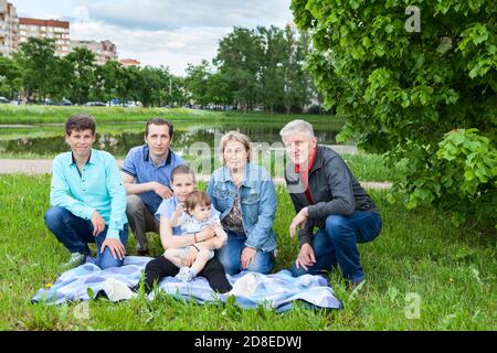Ritratto di famiglia di sei persone durante il fine settimana picnic, nonni anziani, padre singolo adulto, ragazza e ragazzo di età prescolare, ragazza toddler seduta su coperta su un Foto Stock