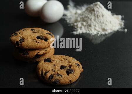 cucina ancora vita cottura processo artigianale biscotti al cioccolato con cioccolato gocce nella farina di fondo e uova di pollo si trovano sopra uno specchio nero all'indietro Foto Stock