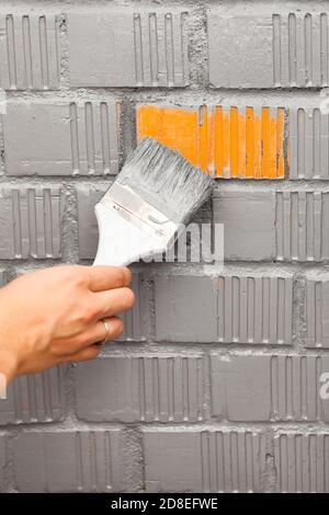 Mano umana pittura ultimo mattone arancione di muro in grigio colore Foto Stock